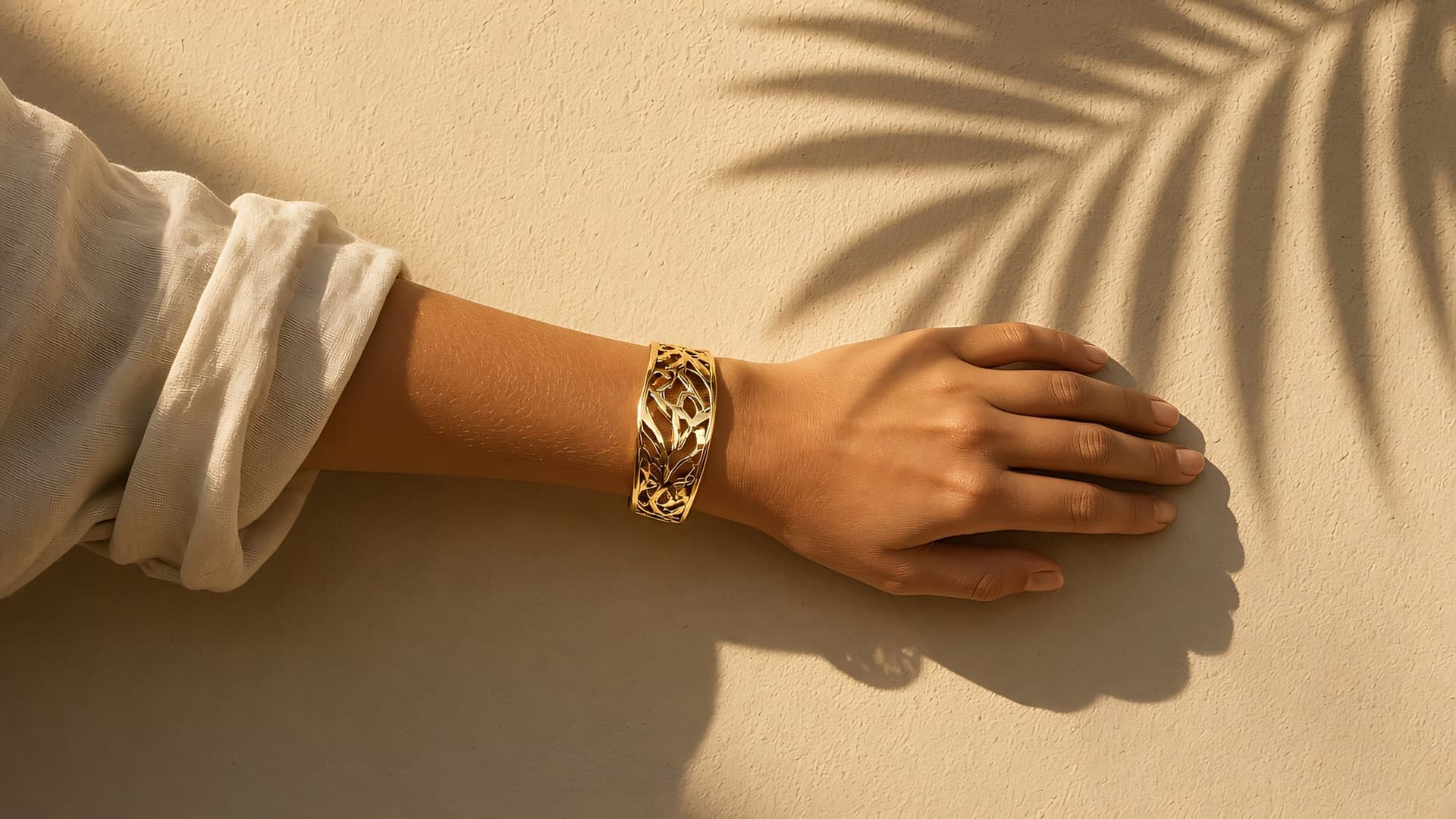 Wrist wearing a gold filigree cuff against a sunlit wall