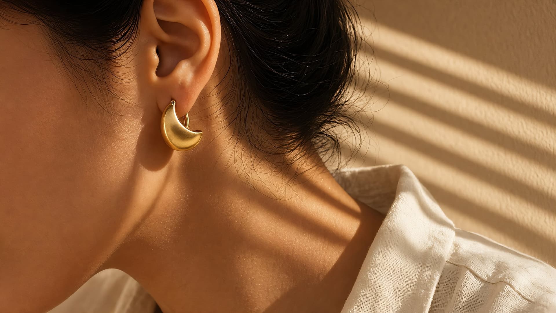 Model wearing a gold dome hoop earring in striped window light