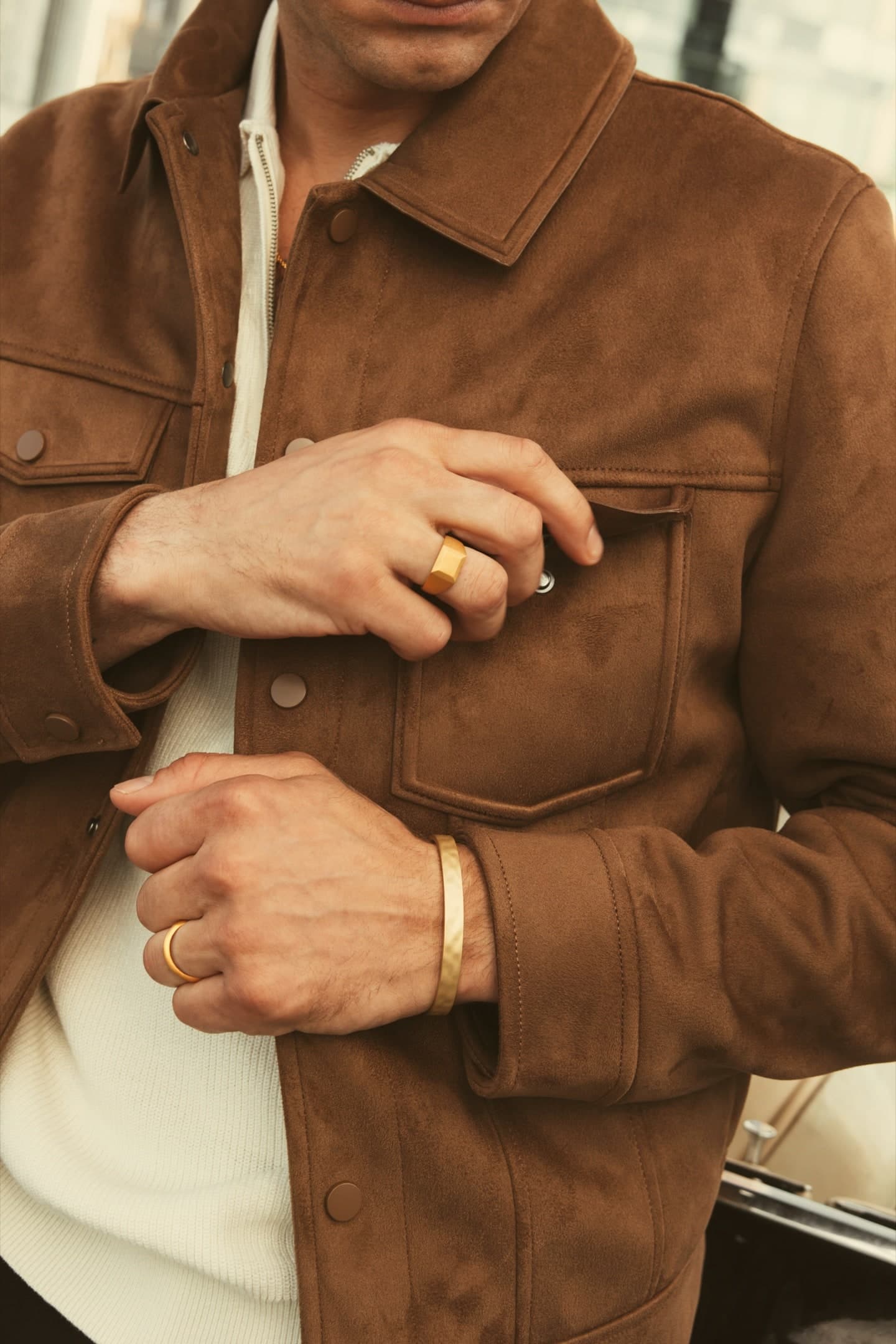 Model in a suede jacket wearing a gold signet ring, a gold band and a hammered gold cuff
