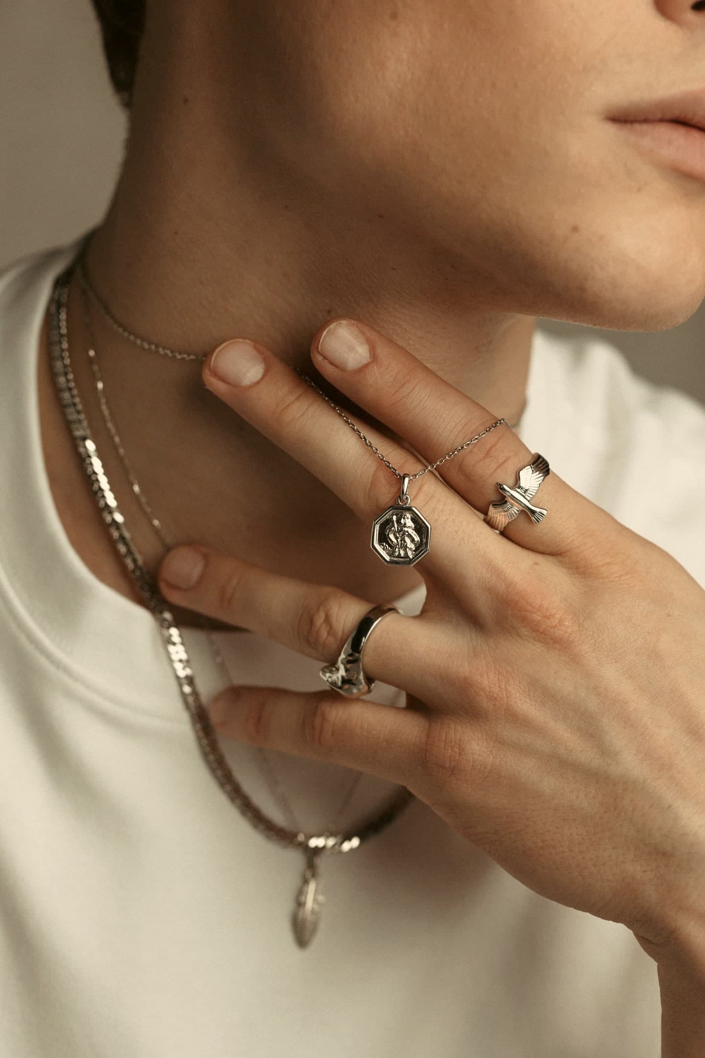 Model wearing a platinum pendant, chains and rings, hand at the neck