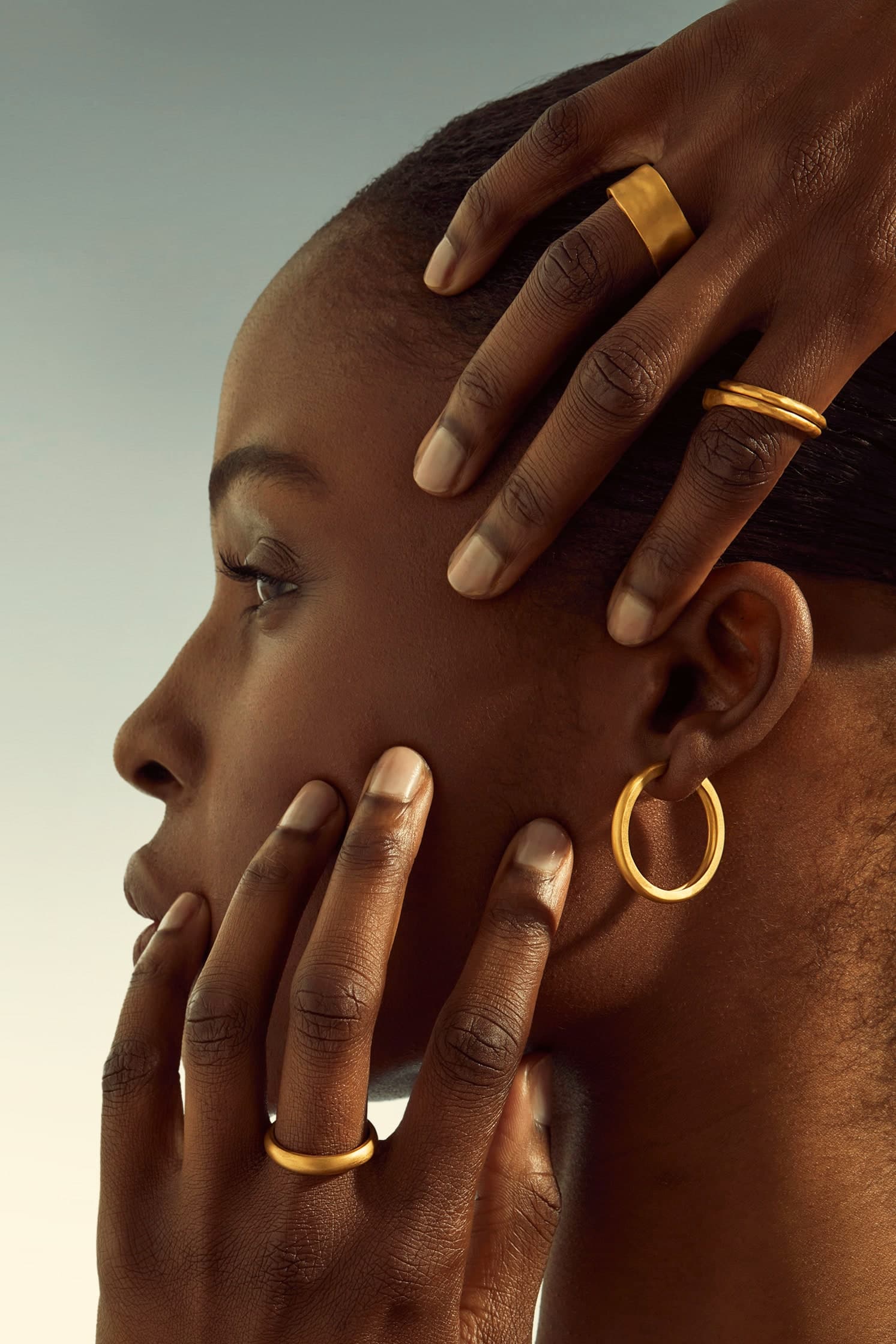 Model wearing gold hoop earrings and stacked gold rings